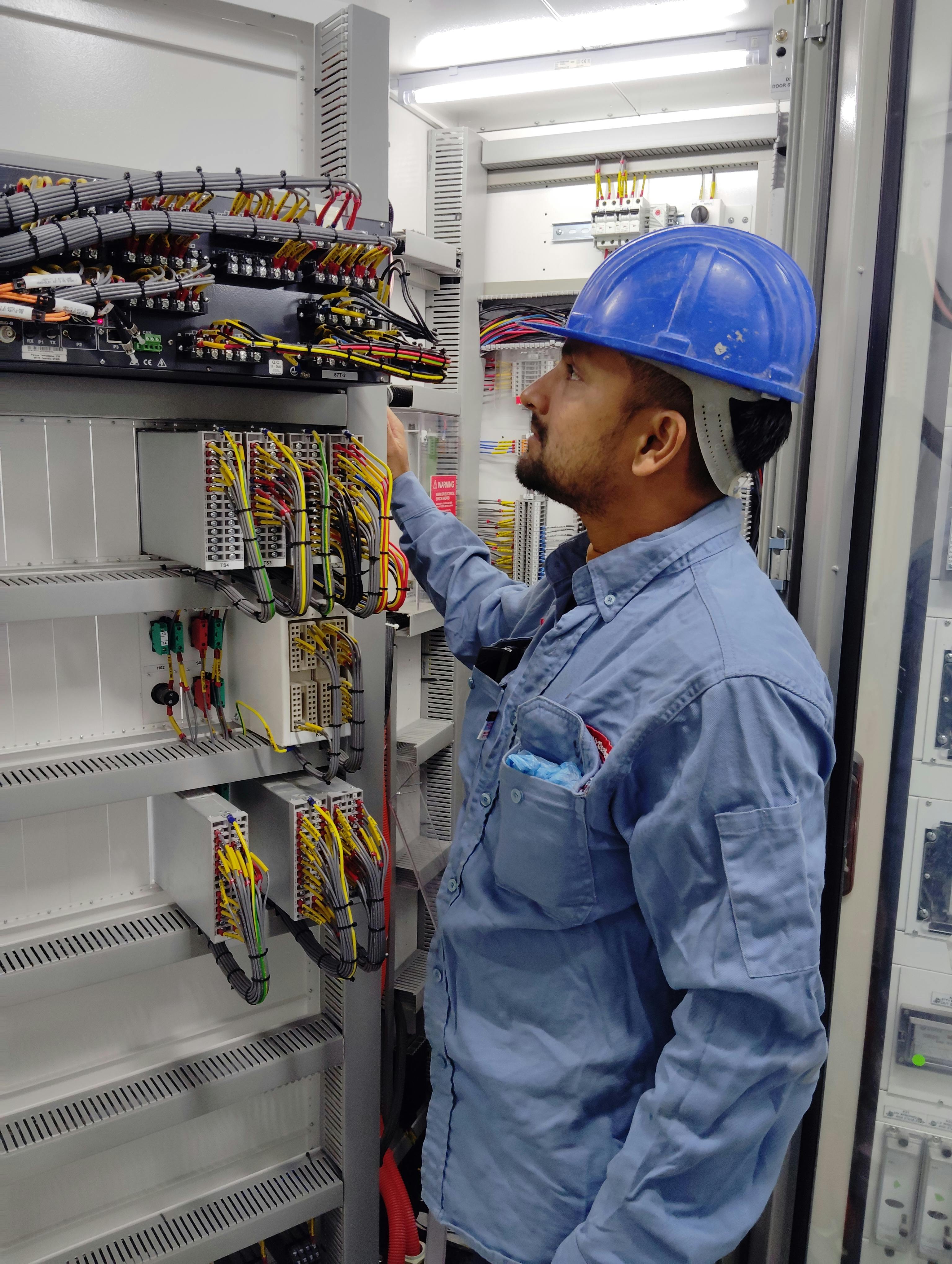 Technician inspecting relay panel wiring in control building